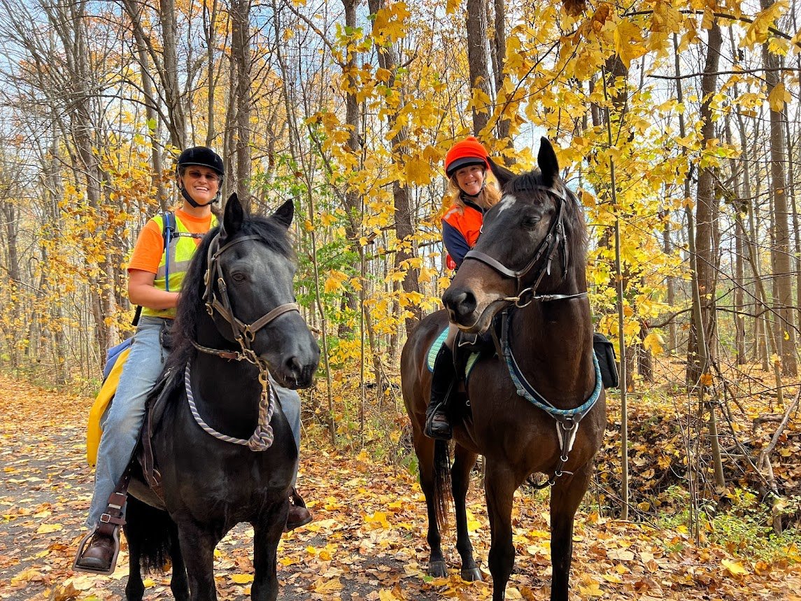 Two equestrians on horseback on an autumn woodland trail.